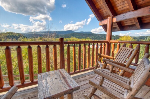 Een houten terras met een tafel en stoelen, met uitzicht op een bergachtig landschap.