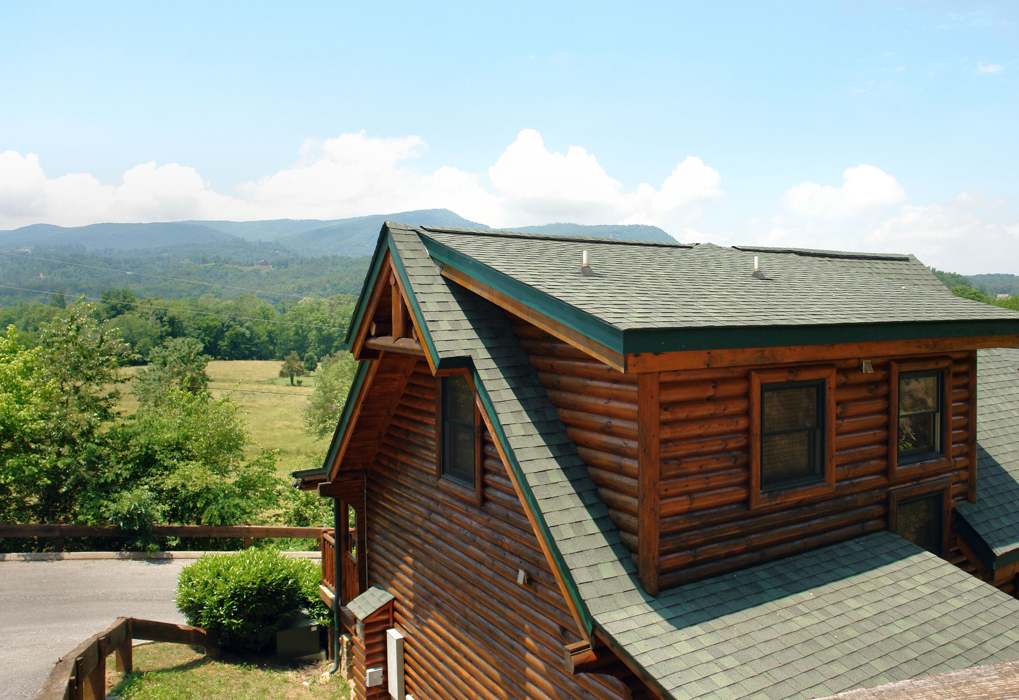 Une cabane en rondins avec un toit en pente, une façade en bois et une vue sur un paysage verdoyant, avec des montagnes en arrière-plan.