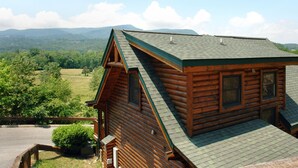Une cabane en rondins avec un toit en pente, une façade en bois et une vue sur un paysage verdoyant, avec des montagnes en arrière-plan.