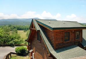 A log cabin with a sloped roof, wooden exterior, and a view of a green landscape with mountains in the background.