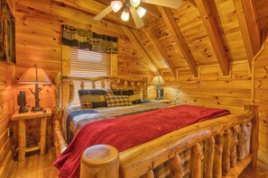 A log cabin bedroom with a wooden bed, a red blanket, and a ceiling fan.