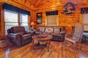 A cozy cabin interior with a leather sofa, a round coffee table, and a wicker chair.