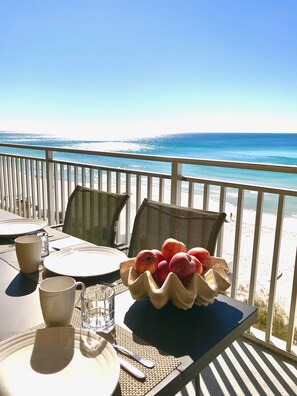 Una mesa para dos con un bol de fruta, un vaso de agua y platos en un balcón con vistas a la playa.