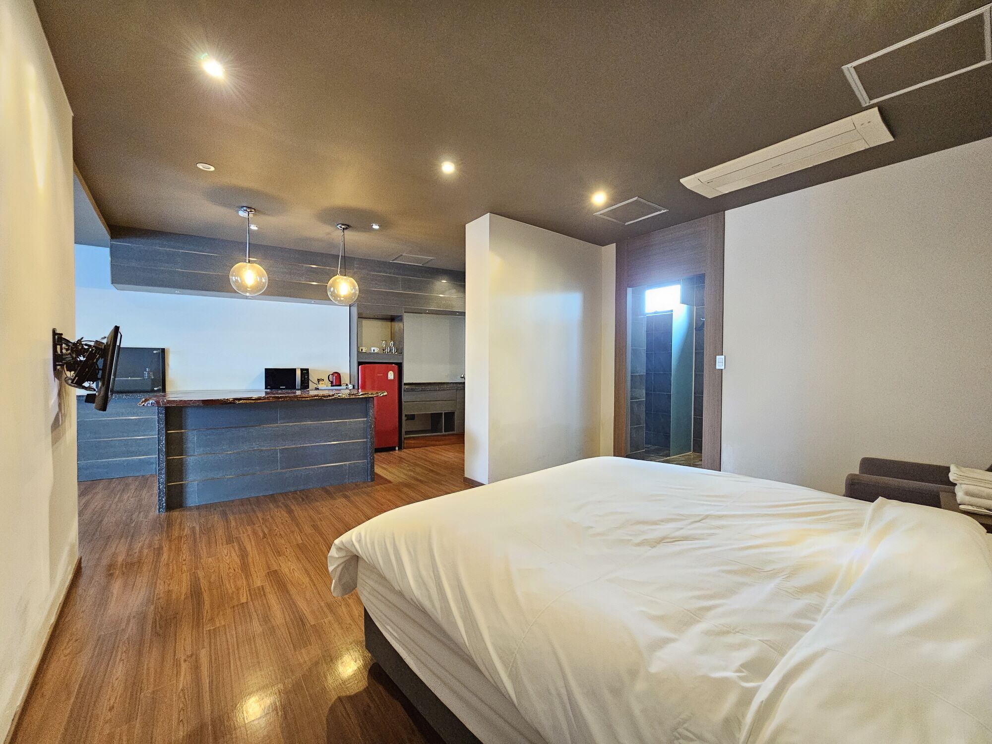 Un dormitorio moderno con una cama grande, una kitchenette pequeña y un baño separado.
