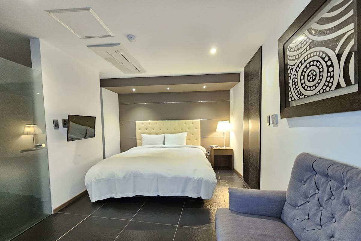 A modern hotel room with a large bed, a grey sofa, and a decorative wall piece.