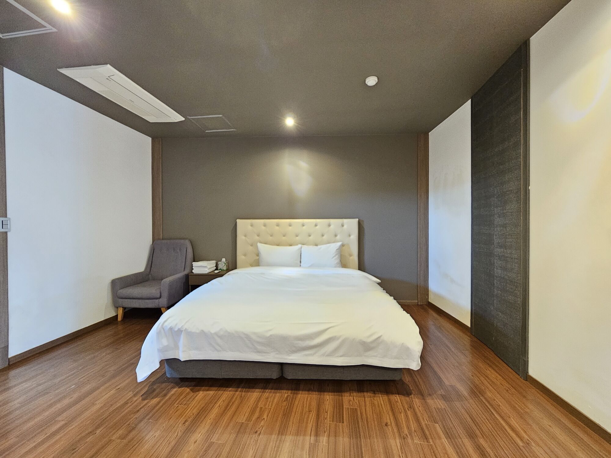 A modern hotel room with a large bed, a chair, and a wooden floor.