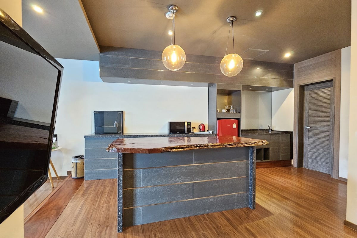 A modern kitchen with a central island, wooden flooring, and pendant lighting.