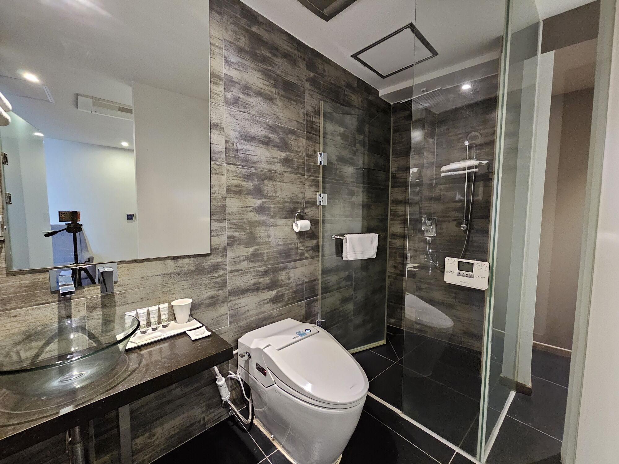 A modern bathroom with a marble vanity, a toilet, a glass shower enclosure, and a large mirror.