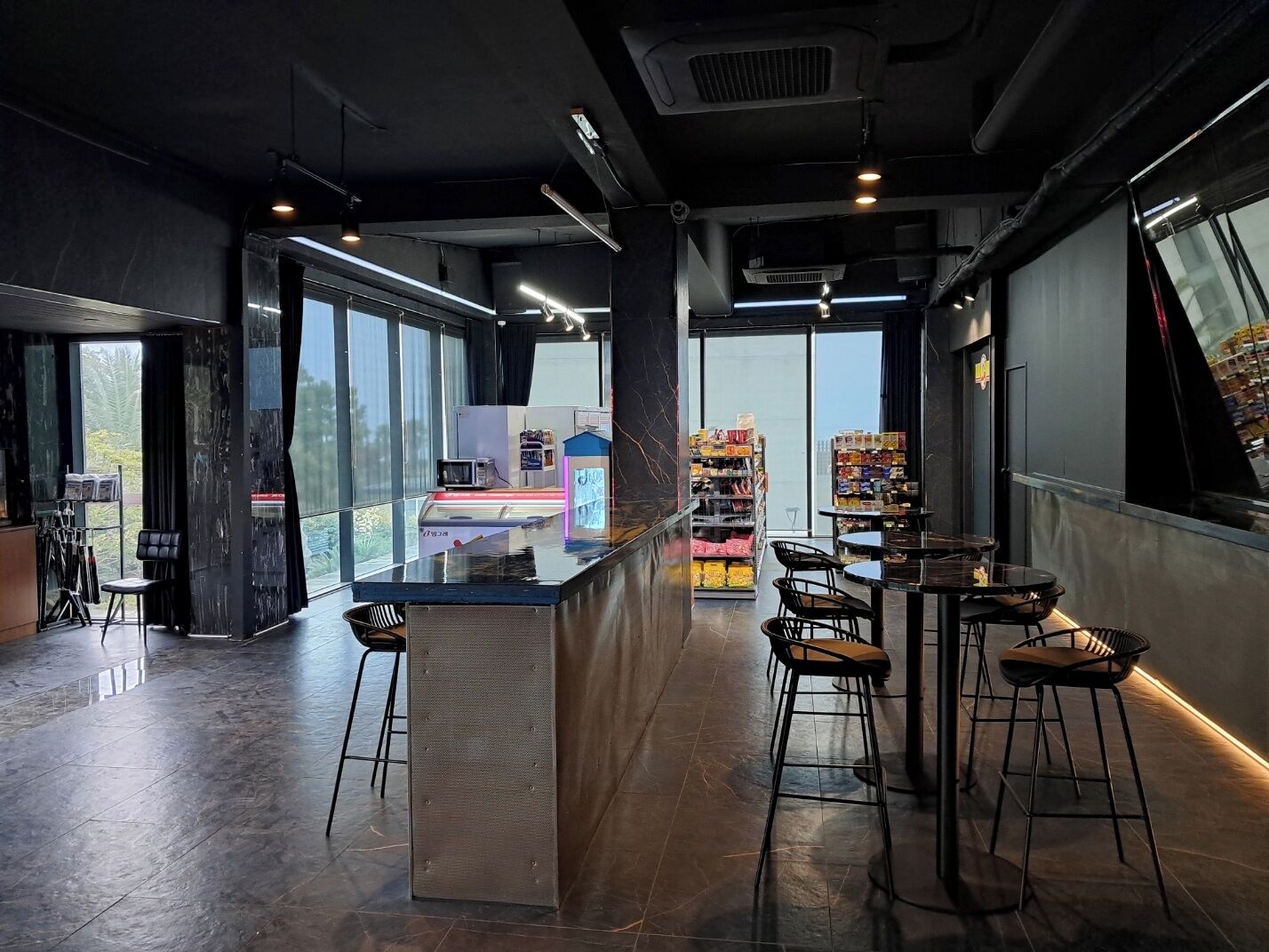 A modern bar area with a counter, stools, and a view of the city through large windows.