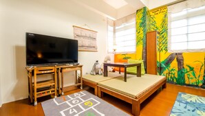 A living room with a television on a wooden stand, a sofa, a small table, and a hopscotch game mat. - Dan Dan House (Tongluo)