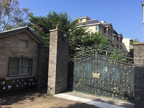 A gated entrance with a stone wall and a metal gate with intricate designs. - Dan Dan House (Tongluo)