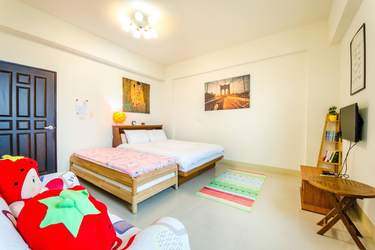 A bedroom with two beds, a wooden wardrobe, a television on a stand, and a small table.