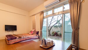 A room with a bed, a table with a tray of cups, a TV mounted on the wall, and a large window with curtains. - Dan Dan House (Tongluo)