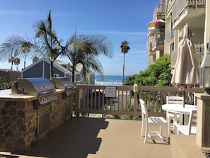 Une terrasse avec un barbecue, des chaises blanches et une vue sur la plage et l’océan.