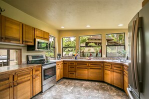 A kitchen with wooden cabinets, a stainless steel refrigerator, a microwave, and a large window overlooking a garden.