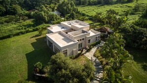 Une maison moderne à plusieurs étages, dotée d’un toit plat, entourée d’une végétation luxuriante et d’une pelouse bien entretenue.