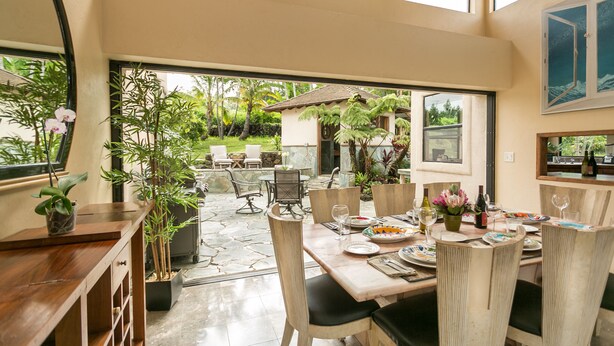 Un coin repas avec une table dressée pour quatre personnes, entourée de chaises, et offrant une vue sur la terrasse et le jardin.