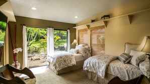 Une chambre avec deux lits, un coin salon avec un fauteuil et une vue sur un jardin, accessible par une porte coulissante.