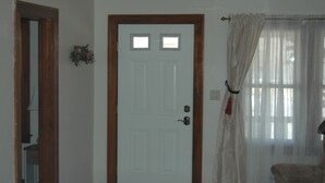 A room with a white door, a red carpet, a wooden-framed mirror, and a window with sheer curtains. - Bethany Bungalow, 2 Bdrm, 1 Bath bungalow near all Husker events (Lincoln)