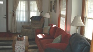 A living room with a red sofa, a beige armchair, a wooden coffee table, and a floor lamp. - Bethany Bungalow, 2 Bdrm, 1 Bath bungalow near all Husker events (Lincoln)