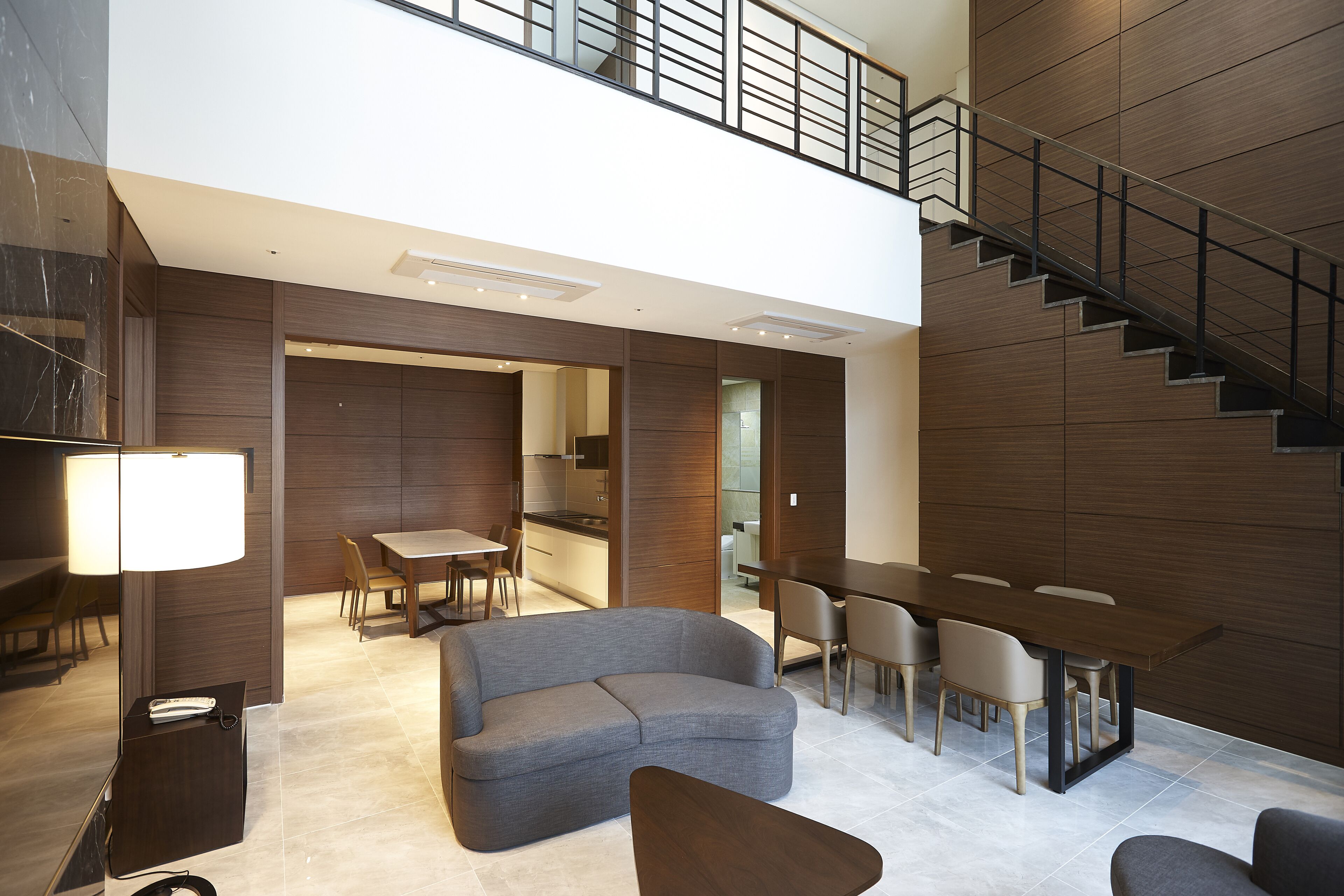 Un interior moderno con un sofá, una mesa de comedor y sillas, una escalera y una zona de cocina.