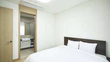 Una habitación de hotel con cama, puerta de madera, baño con lavamanos y espejo, e iluminación en el techo.