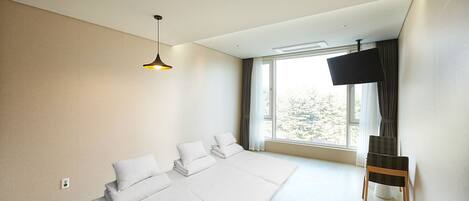 Una habitación de hotel moderna con una cama grande, televisión y ventana con vistas a árboles.
