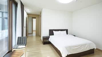 A modern hotel room with a large bed, a chair, a small table, and a view through a large window.