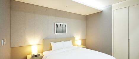 A modern hotel room with a large bed, bedside lamps, a framed artwork above the bed, and a wardrobe.