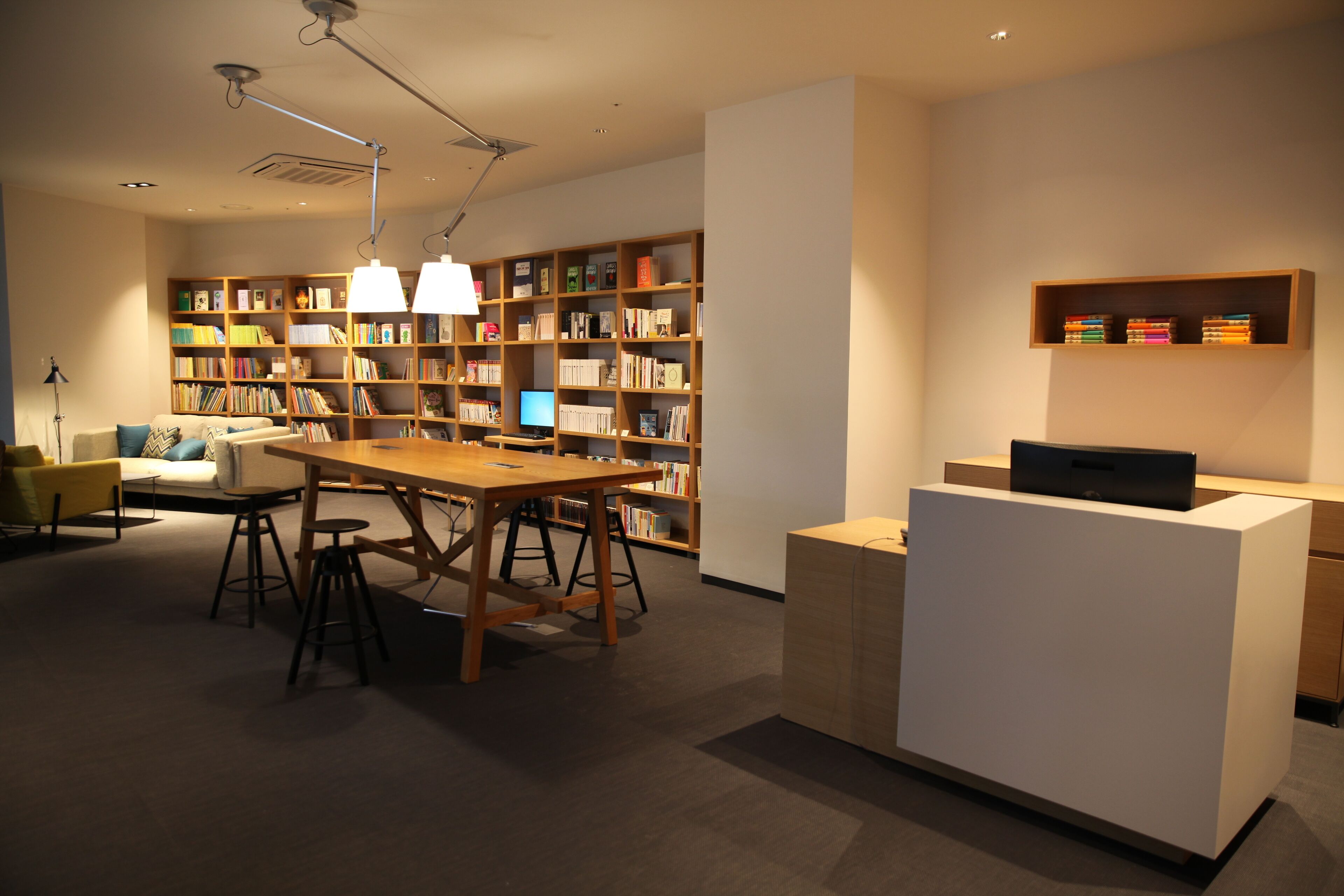 A modern library with a wooden table, bookshelves, and a white reception desk.
