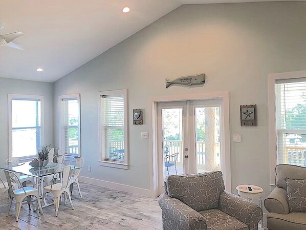 A spacious living room with a glass dining table, white chairs, and a patterned sofa.