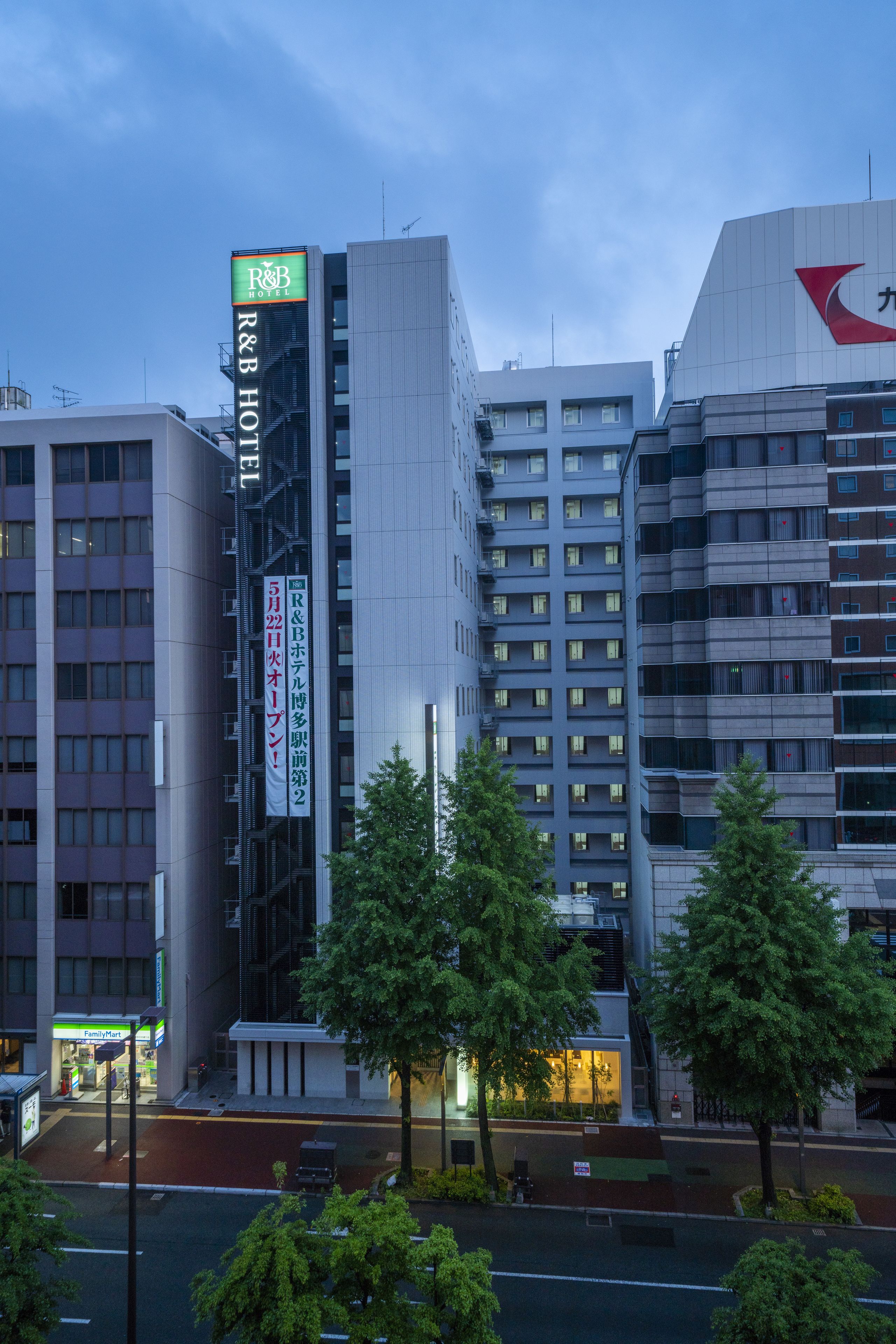 Un hôtel à plusieurs étages, avec une enseigne bien visible indiquant « R&B Hotel », et un logo en forme de flèche rouge sur le côté.
