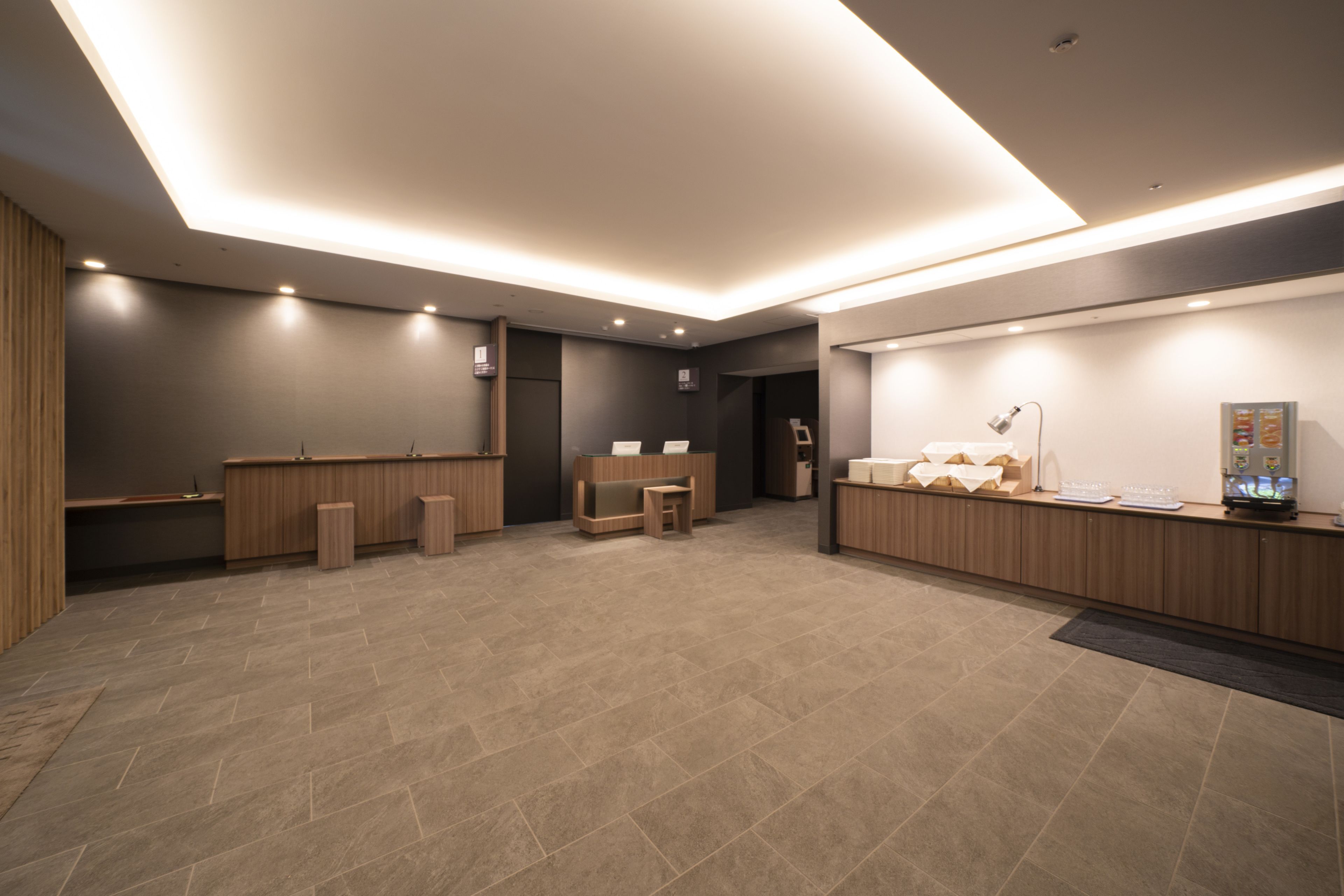 A modern reception area with a wooden reception desk, a waiting area with a bench, and a counter with a computer and a display.