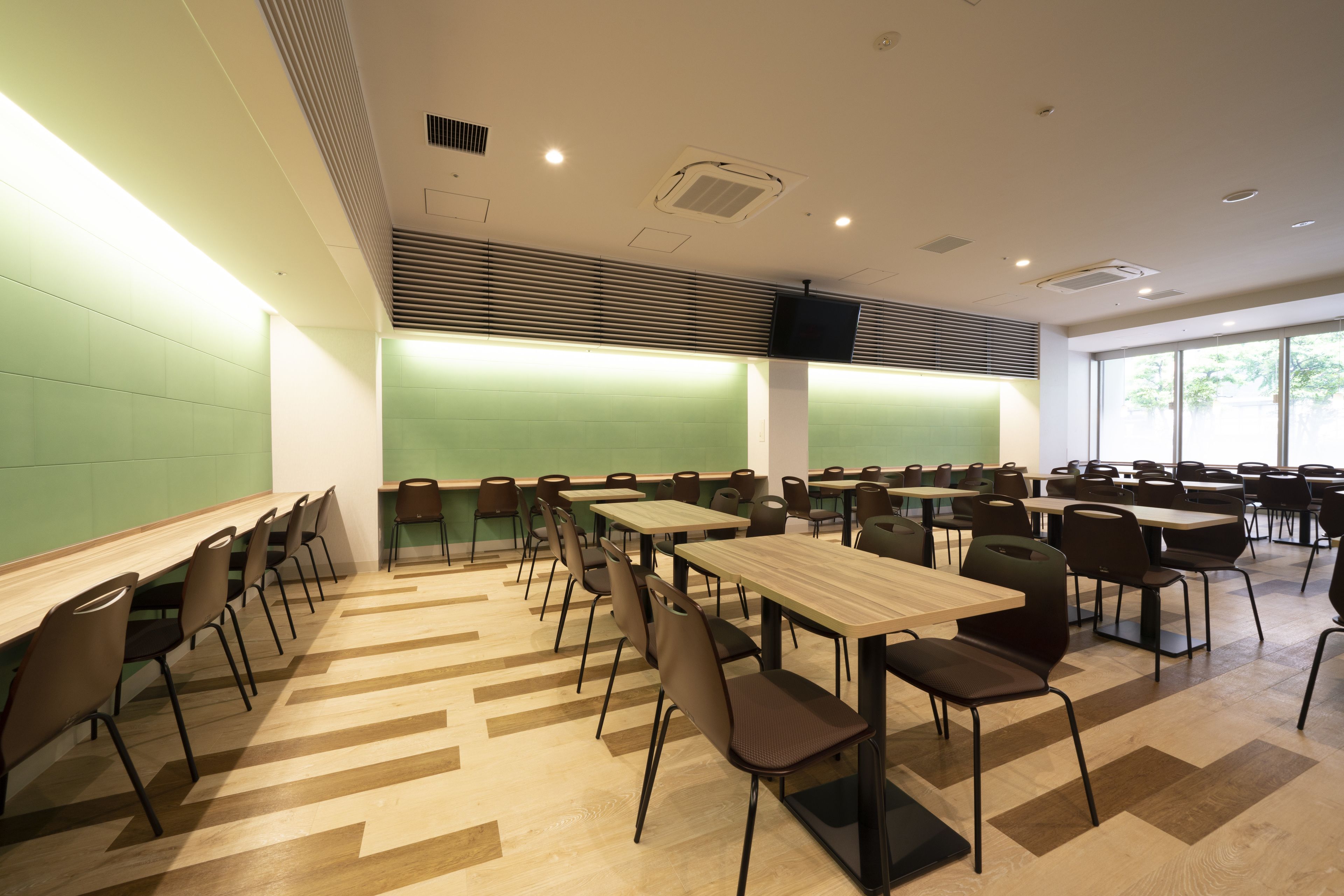 A modern conference room with multiple tables and chairs, a green accent wall, and large windows.