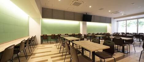 A modern conference room with multiple tables and chairs, a green accent wall, and large windows.