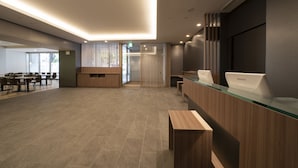 Ein moderner Hotel-Empfangsbereich mit Glastresen, Holztresen und einer Sitzecke mit Tischen und Stühlen.