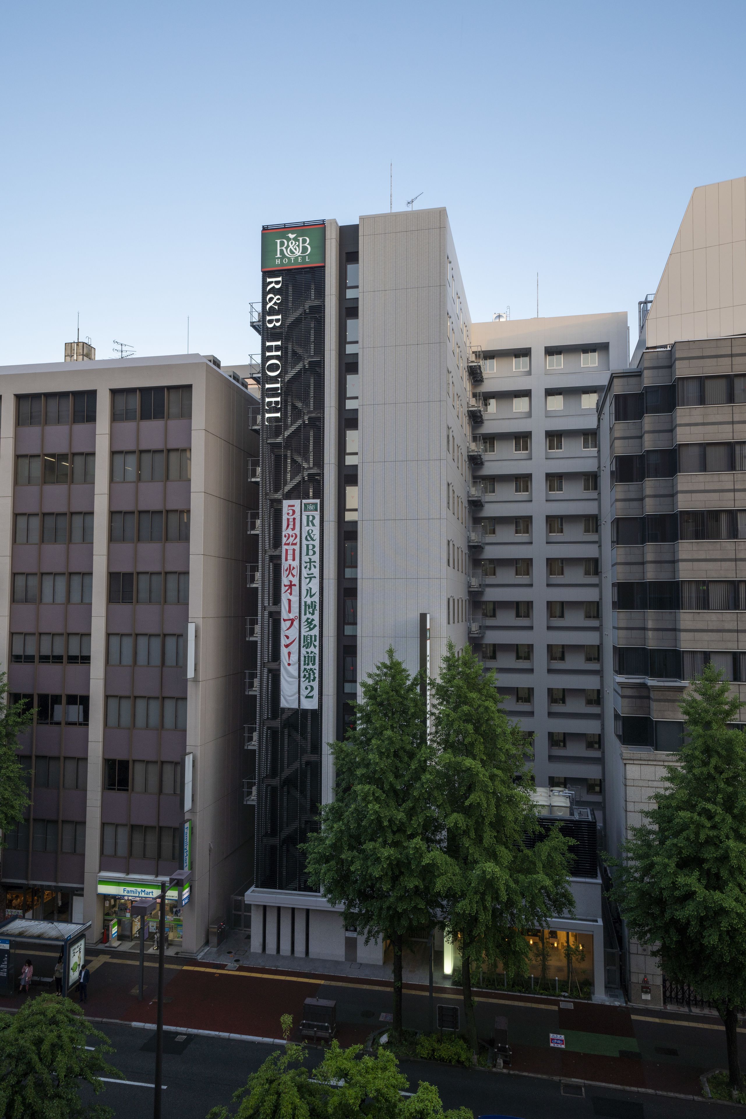 A multi-story hotel with a prominent R&B Hotel sign, surrounded by other buildings and trees.