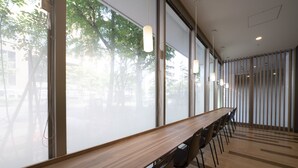 Ein Konferenzraum mit einem langen Holztisch, Stühlen, großen Fenstern und Blick auf Bäume draußen.