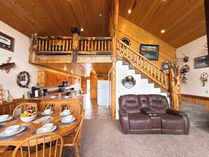 A rustic cabin interior with a dining area, a leather sofa, a staircase, and a kitchen.