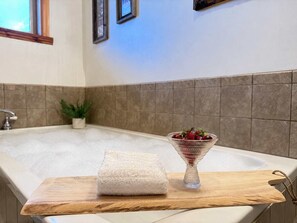 Eine Badewanne mit einem hölzernen Tablett, das ein weißes Handtuch und eine Schale mit Kirschen trägt.