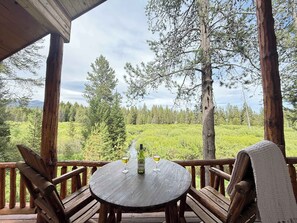 A wooden deck with a round table, two chairs, and a bottle of wine.