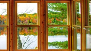 A room with multiple windows reflecting a forest and a lake.