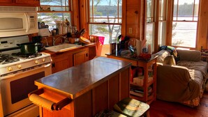 A cozy cabin interior with wooden walls, a kitchen area including a stove, sink, and microwave, and a seating area with a couch and a table.