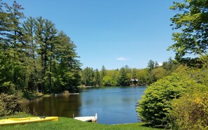 A lakeside view with a dock, a yellow kayak, and a cabin in the background.