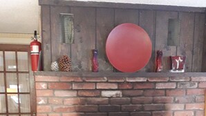A fireplace with a brick surround, a red decorative plate, and a fire extinguisher to the left. - Idyllic Lakefront House Suited Two  Families (Ludlow)