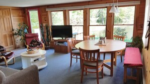 A cozy room with a wooden interior, a round dining table, and a flat-screen TV. - Idyllic Lakefront House Suited Two  Families (Ludlow)
