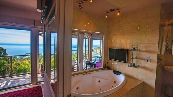 Une salle de bain moderne avec une grande baignoire, un téléviseur et une vue sur l’océan.