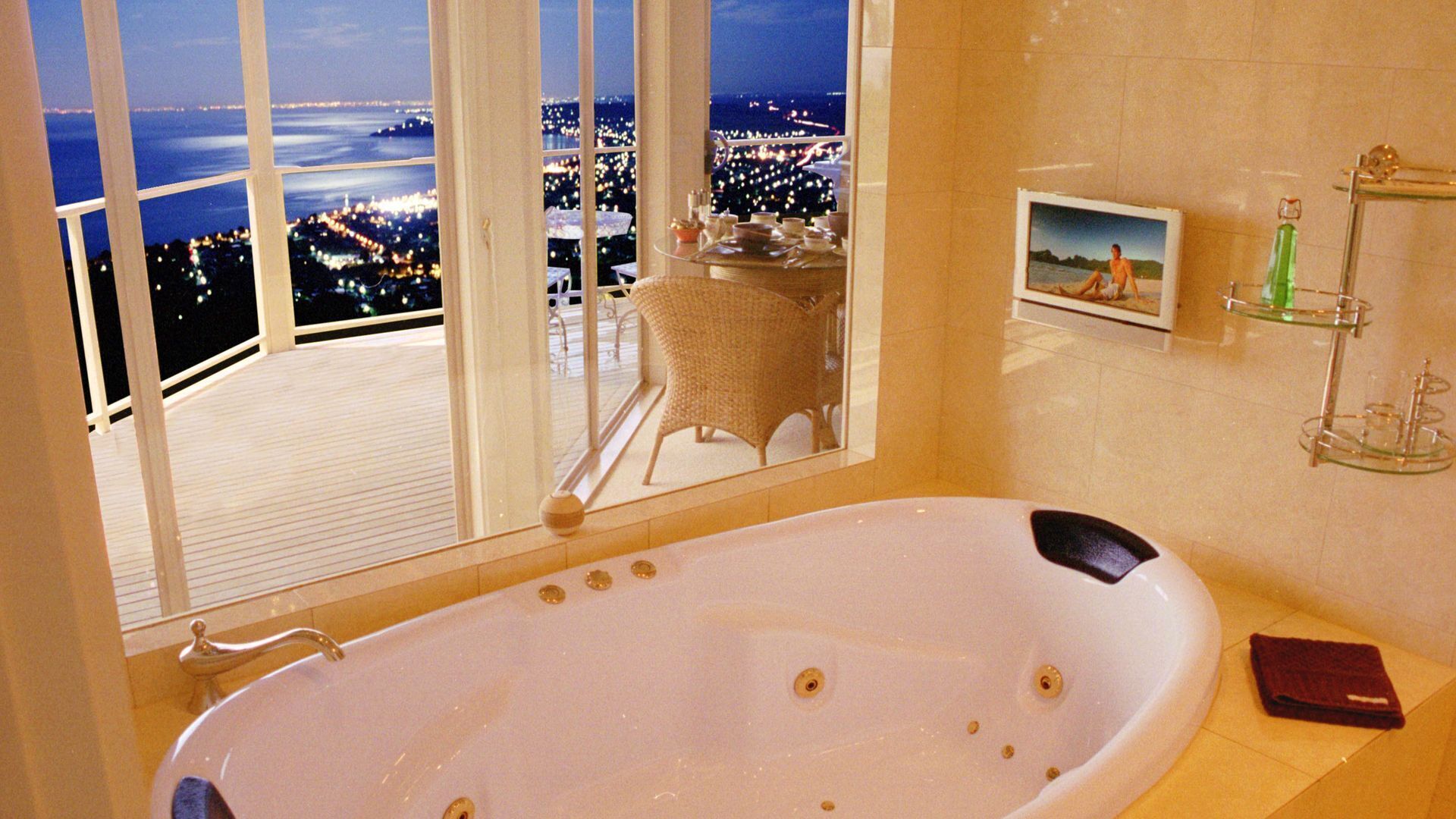 Une salle de bain avec une grande baignoire, une vue sur le paysage urbain par la fenêtre et une petite table avec une chaise.