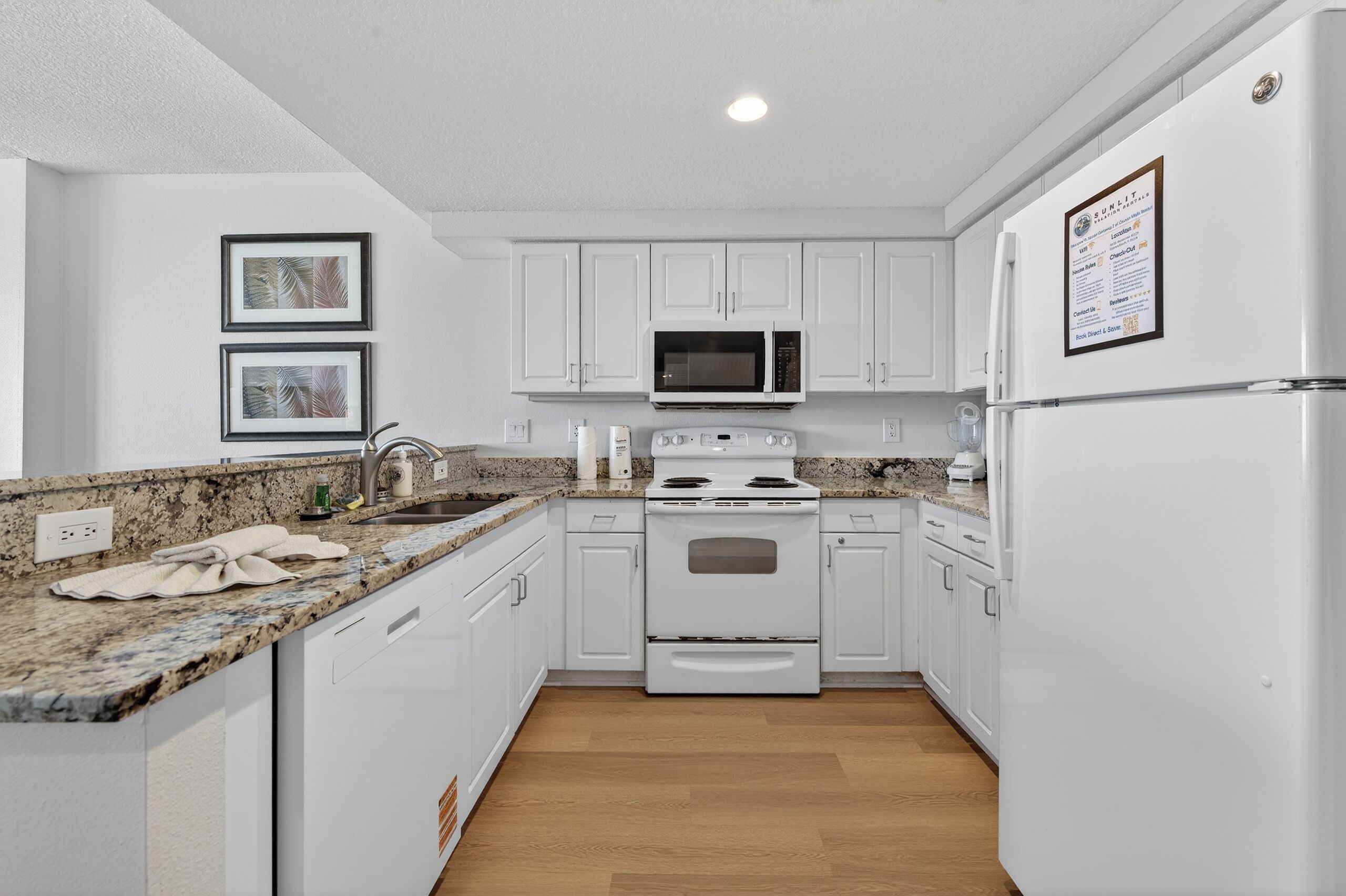A modern kitchen with white cabinets, a granite countertop, a stove, a microwave, and a refrigerator.