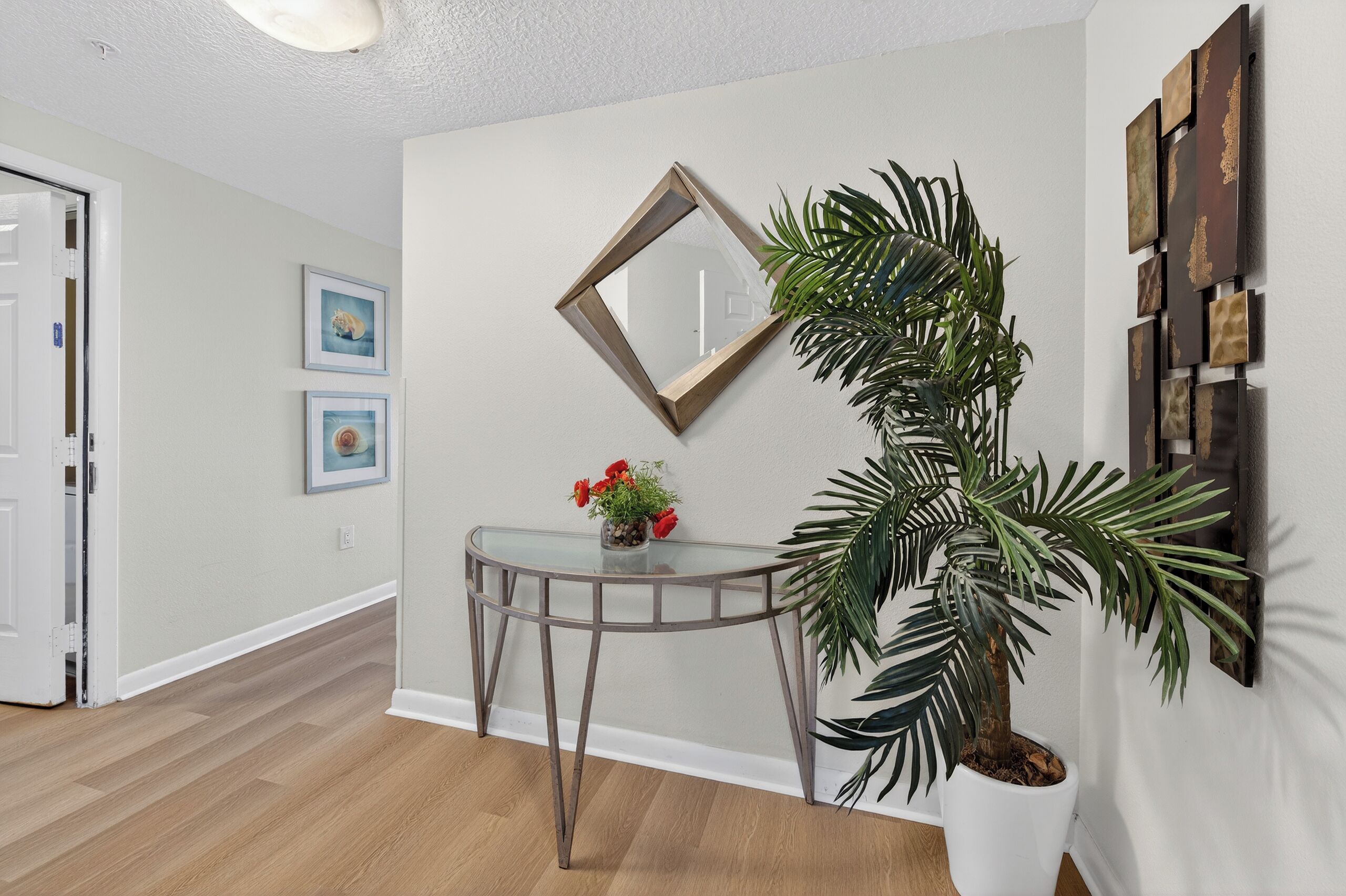 A hallway with a glass table, a potted plant, and a wall-mounted mirror.
